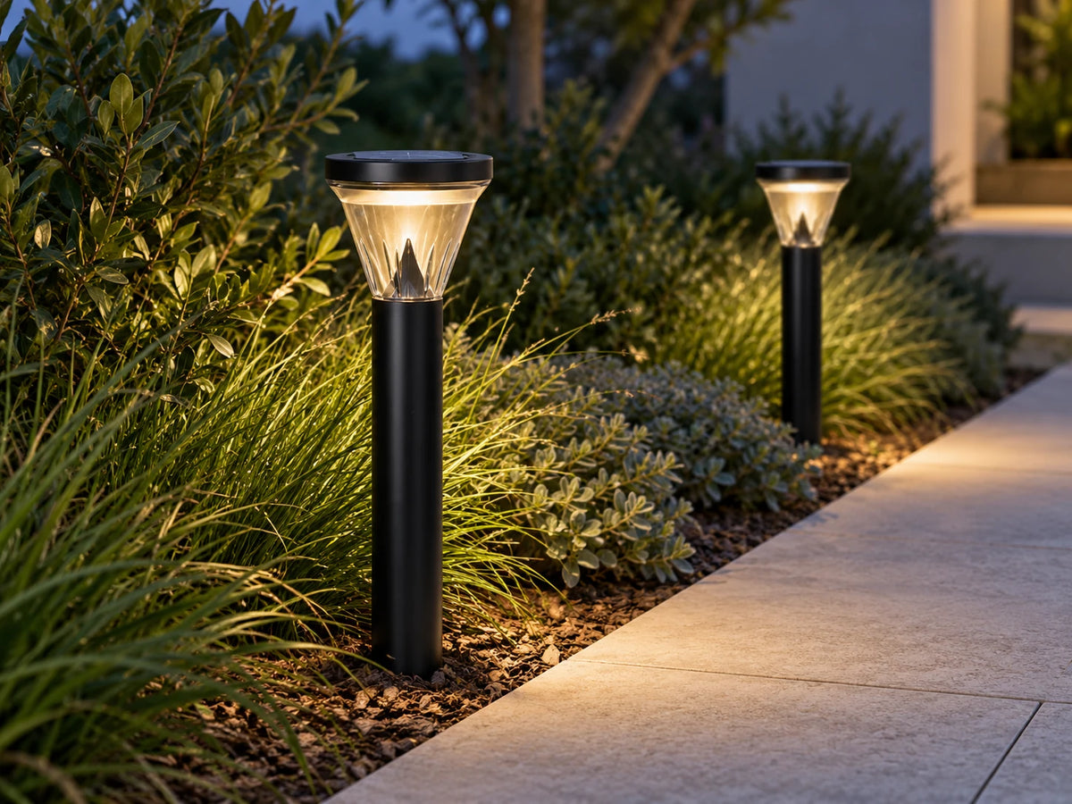 Two black Solar Lighting Direct SLDBL0026 solar bollards beside a garden pathway at dusk